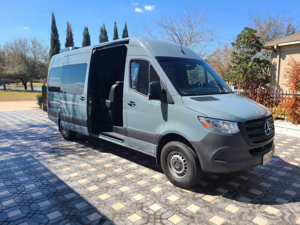 Gray Mercedes-Benz Sprinter van with sliding door open, parked on a paver driveway on a sunny day