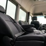Interior of a passenger van with black leather seats, seatbelts, and large windows along the cabin