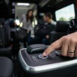 Driver's hand pressing an illuminated control button on a van's center console, with passengers visible in the background